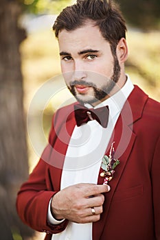 Portrait of groom in red suit with a bow tie, beard and mustache.