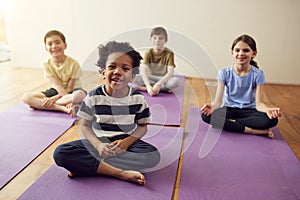 Portrait Of Group Of Children Sitting On Exercise Mats In Exercise Class
