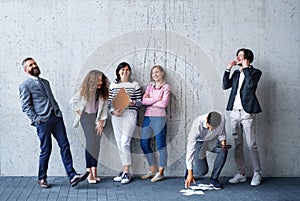 Portrait of group of entrepreneurs standing against concrete wall indoors in office, laughing.