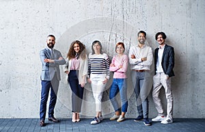 Portrait of group of entrepreneurs standing against concrete wall indoors in office, looking at camera.