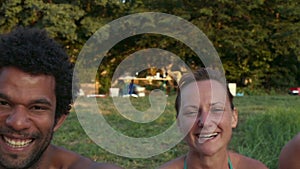 Portrait of group of friends sitting in nature at sunset, laughing at camera