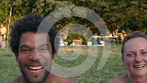 Portrait of group of friends sitting in nature at sunset, laughing at camera