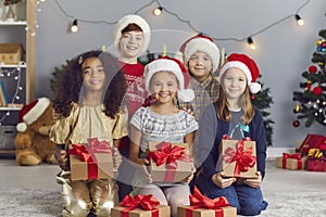 Portrait of a group of happy smiling international children holding Christmas presents in a room.