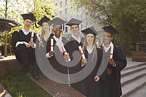 Portrait of a group laughing happy multiracial graduates holding diploma outdoor.