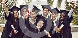 Portrait of a group laughing happy multiracial graduates holding diploma outdoor.