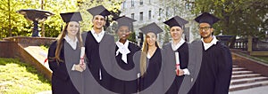 Portrait of a group smiling happy multiracial graduates holding diploma outdoor. Banner.