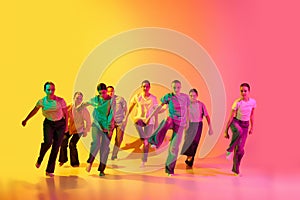 Portrait with group of teenagers, young dancers jumping together over pink and yellow gradient background in neon light