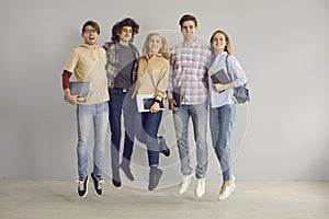 Portrait of a group of young cheerful girls and boys students jumping on a gray wall background.