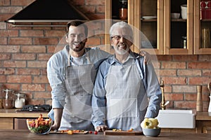 Portrait of grown son hugging mature father cooking at kitchen