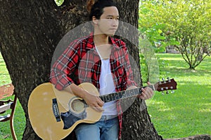 Portrait of guitarist playing music on acoustic guitar in the park background.