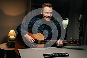 Portrait of guitarist singer man emotionally singing into condenser microphone and playing acoustic guitar in dark home