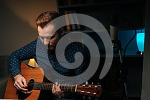 Portrait of guitarist singer man play on acoustic guitar recording sing song using condenser microphone stand in dark