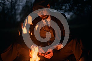 Portrait of a guy sitting by the fire at night in nature. Cinematic vintage photo. Retro 1920s portrait of an English man with a