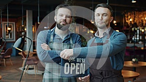 Portrait of guys in aprons changing closed to open sign in modern cafe smiling