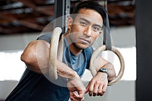Portrait, gymnastic rings and olympics with a man gymnast hanging on equipment for workout in gym. Face, fitness and