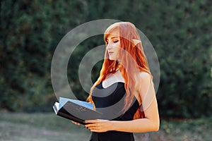 portrait of Halloween Beautiful young Witch woman on forest background with magic Book of spells.