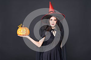 Portrait of Halloween Witch girl, Beautiful young Asian women  holding carved pumpkin over black background