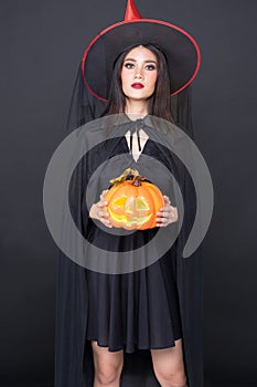 Portrait of Halloween Witch girl, Beautiful young Asian women  holding carved pumpkin over black background