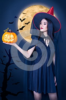 Portrait of Halloween Witch girl, Beautiful young Asian women  holding carved pumpkin over moon background