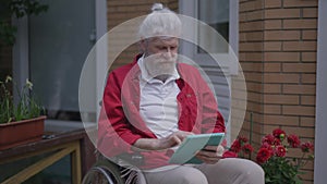 Portrait of handicapped bearded senior Caucasian man surfing social media on tablet in slow motion smiling. Disabled