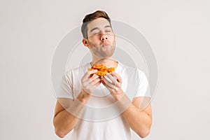 Portrait of handome young man with enjoying eating delicious slice of pizza, with closed eyes from pleasure on white