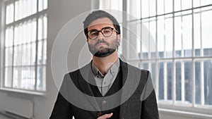 Portrait of handsome adult man with beard and eyeglasses dressed in business suit in modern building