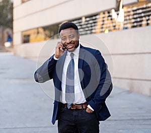 Portrait of handsome african american businessman walking in the city talking on mobile phone