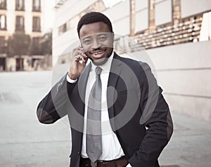 Portrait of handsome african american businessman walking in the city talking on mobile phone