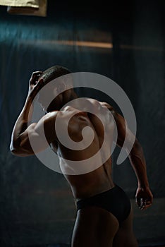 Portrait of handsome african american male body builder with naked torso posing on a black studio background.