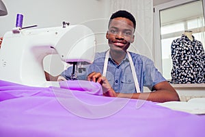 Portrait of a handsome african man smiling seamstress with sewing machine working in tailor workshop mannequin,table