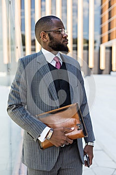 Portrait of handsome afro american businessman using phone in suit against modern building exterior. reflection in glass