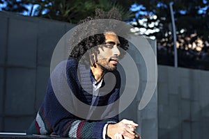 Portrait of handsome Afro American man in casual clothes, looking away and laughing while leaning on a fence, standing outdoors