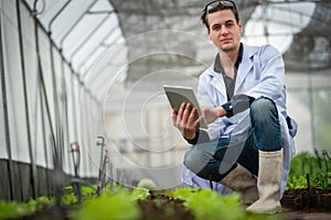 Portrait of handsome agricultural researcher holding tablet while working on research at plantation in industrial greenhouse