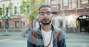 Portrait of handsome Arab guy in glasses standing outdoors with serious face