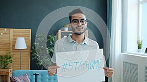 Portrait of handsome Arab man standing at home with stayhome poster during covid-19 outbreak