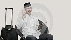 Portrait of handsome asian muslim man with head cap sitting on couch and using tab