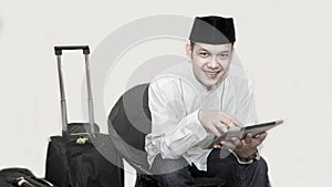 Portrait of handsome asian muslim man with head cap sitting on couch and using tab