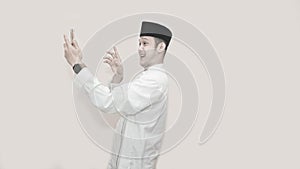 Portrait of handsome asian muslim man with head cap and using smartphone taking a video call and waving smile at phone