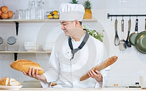 Portrait handsome Asian professional male chef wearing white uniform, hat, showing, holding baguette, bread, cooking breakfast in