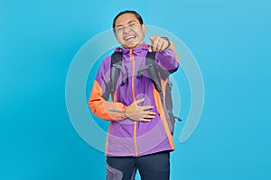 Portrait of handsome Asian young man laughing widely and pointing finger in front isolated on blue background