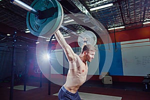 Portrait of a handsome athlete . Athlete raises the barbell over your head. shots in the dark tone. Cross fit style