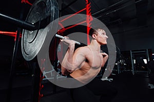 Portrait of a handsome athlete at gym. man does the exercise with barbell, standing and squatting. big confident