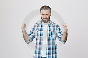 Portrait of handsome athletic adult male showing power and muscles while wearing plaid shirt, standing over gray