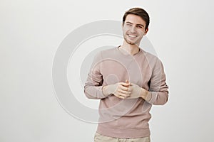 Portrait of handsome athletic male with charming smile holding hands near chest, standing in casual post as if talking