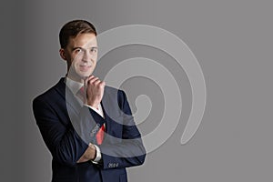 Portrait of handsome, attractive man in blue suit and red tie on grey background