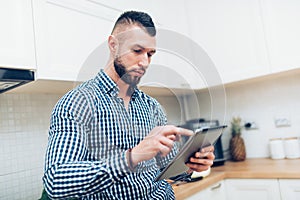 Portrait of handsome, attractive man looking recipes on internet. Man using new technology, working on internet with tablet