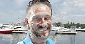 Portrait of handsome attractive man smiling at a lake with boats background. Close up of a happy man smiling at sunny