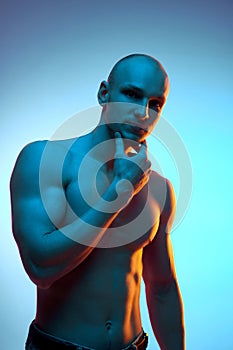 Portrait of handsome, bald, muscular young man standing with shirtless relief body, posing against blue studio