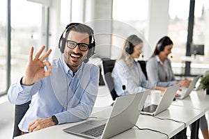 Portrait of handsome bearded business man with headset showing OK sing at call center office