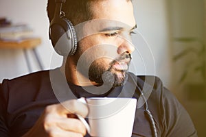 Portrait of handsome bearded man in headphones listening to music at home and drinking coffee. Relaxing and rest time